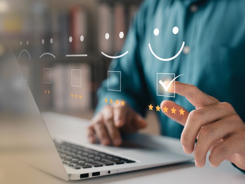 Immagine simbolica della soddisfazione del cliente: una mano su un laptop assegna una valutazione digitale di cinque stelle con un'icona sorridente.